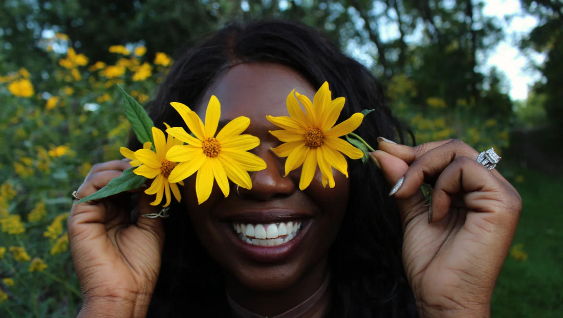 Smiling woman holding yellow flowers over her eyes in a green garden setting