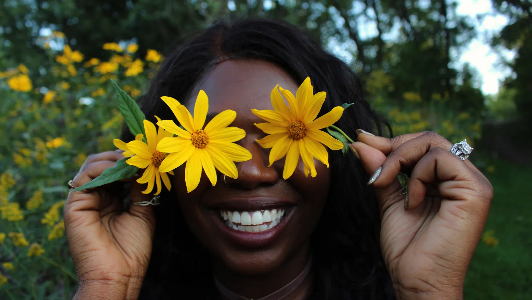 Smiling woman holding yellow flowers over her eyes in a green garden setting