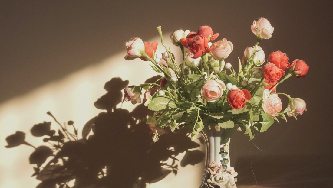 Ceramic vase with pink and red artificial roses casting shadows on beige wall