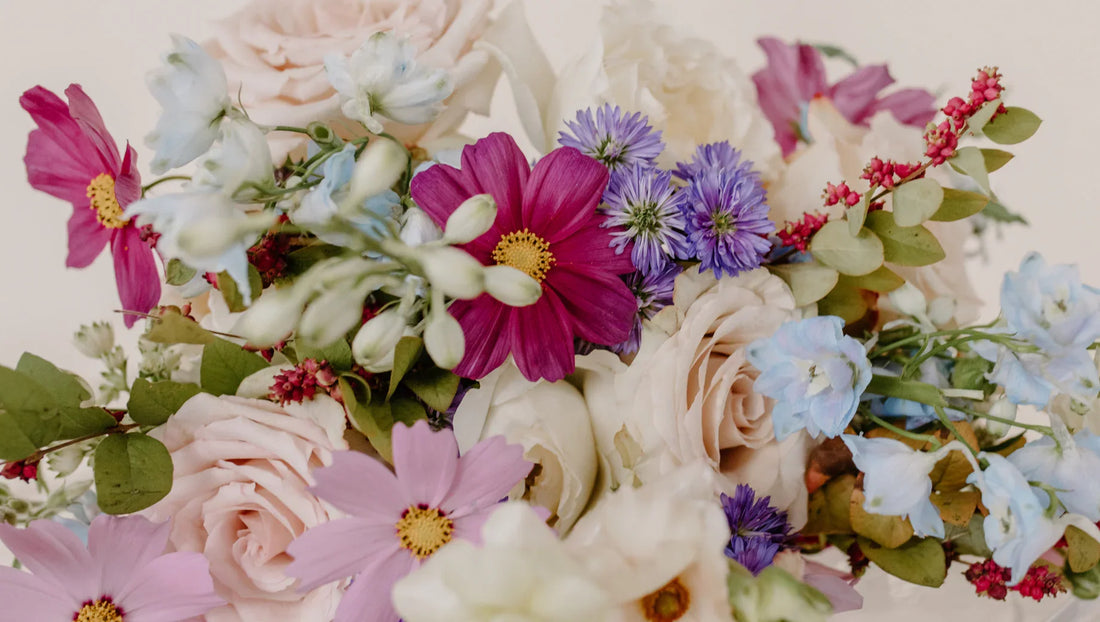 Colorful flower bouquet featuring pink cosmos, pale roses, blue cornflowers, and greenery