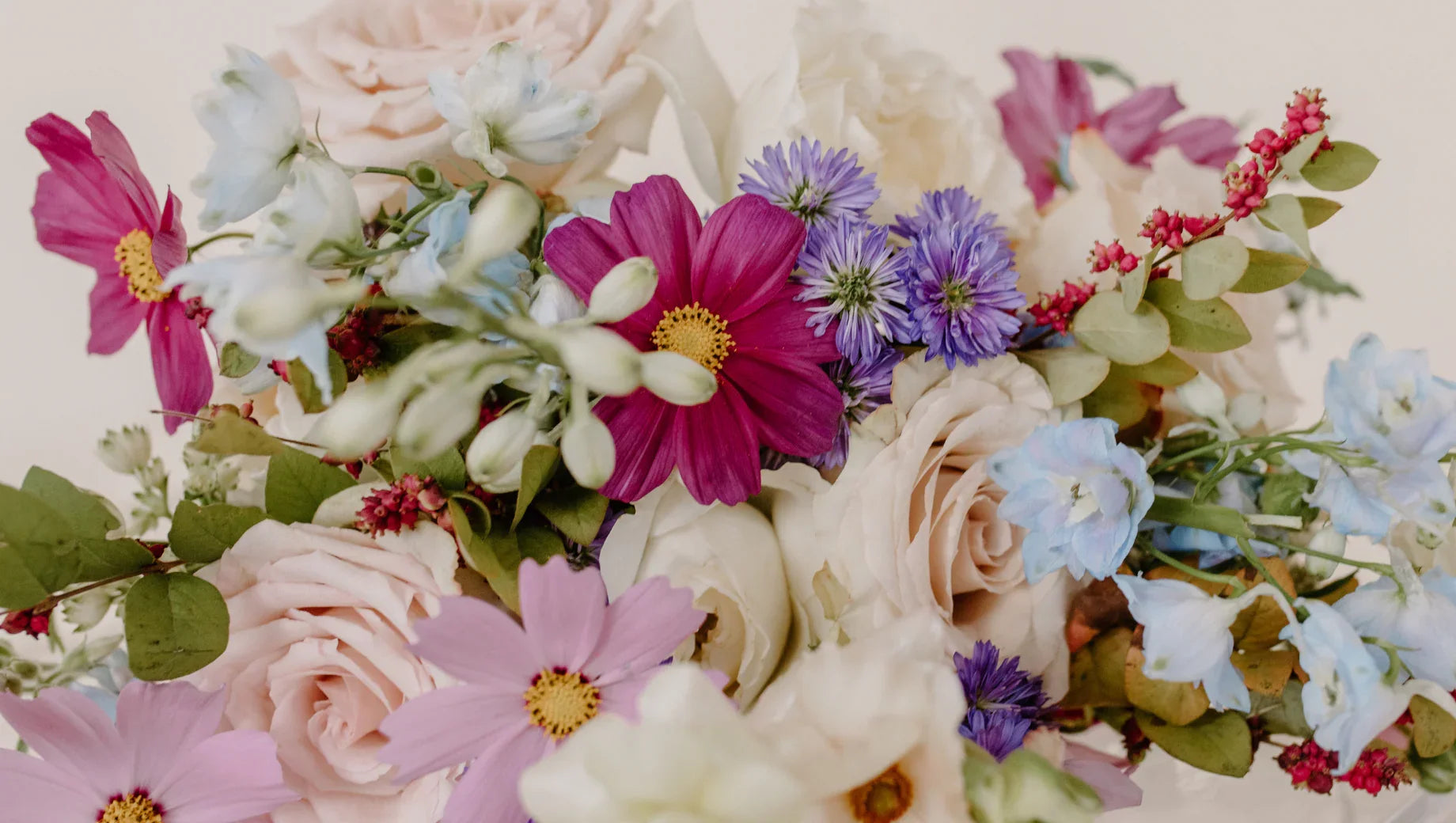 Colorful flower bouquet featuring pink cosmos, pale roses, blue cornflowers, and greenery