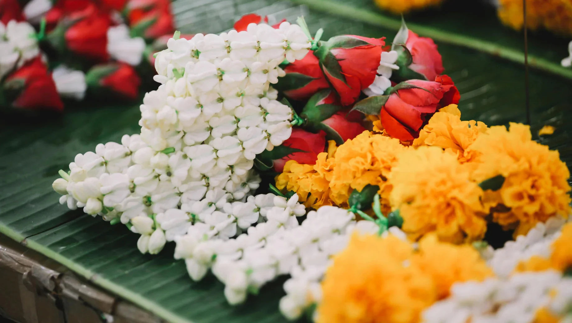 Close-up of white jasmine, red rose buds, and yellow marigold flowers on green banana leaves
