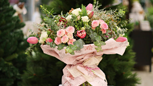 Elegant bouquet of pink roses, tulips, and eucalyptus wrapped in decorative paper with burlap bow