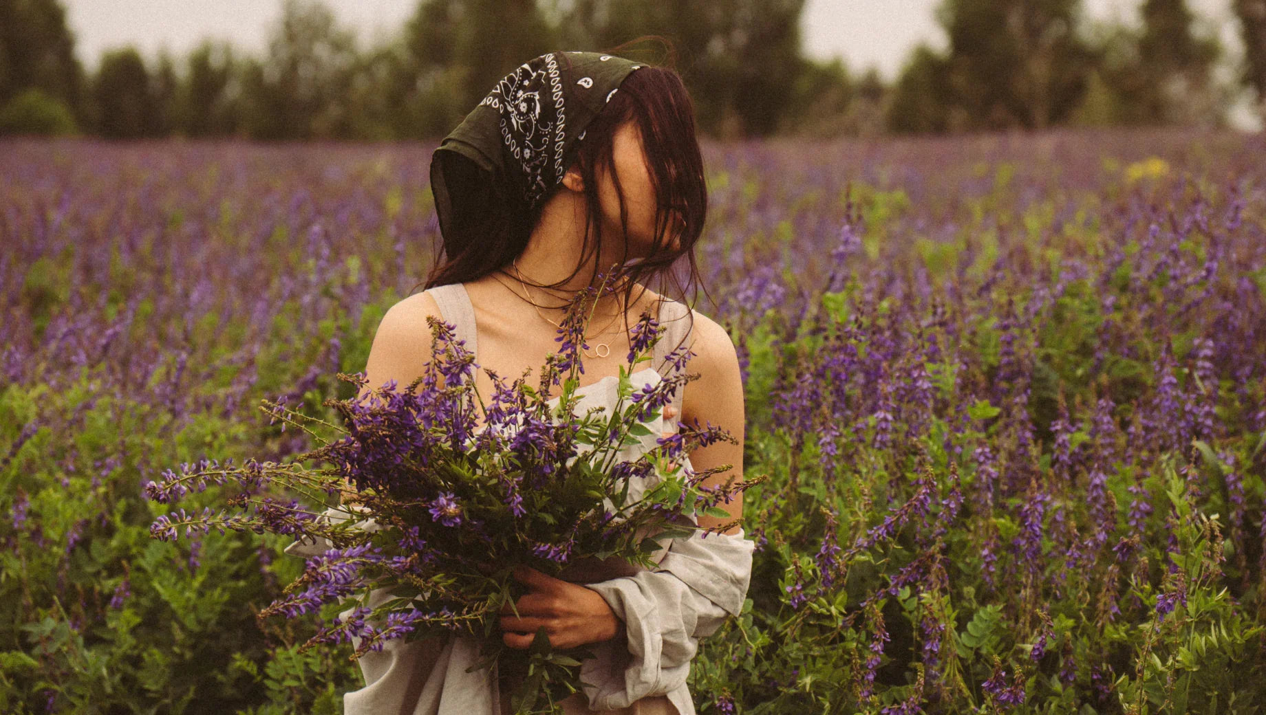 Woman with dark hair and bandana holding purple wildflowers in a blooming lavender field