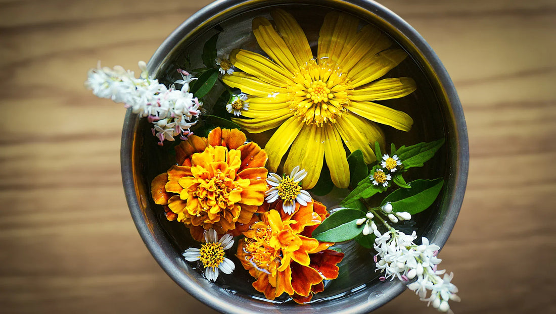 Colorful orange, yellow, white flowers floating in metal bowl on wooden surface