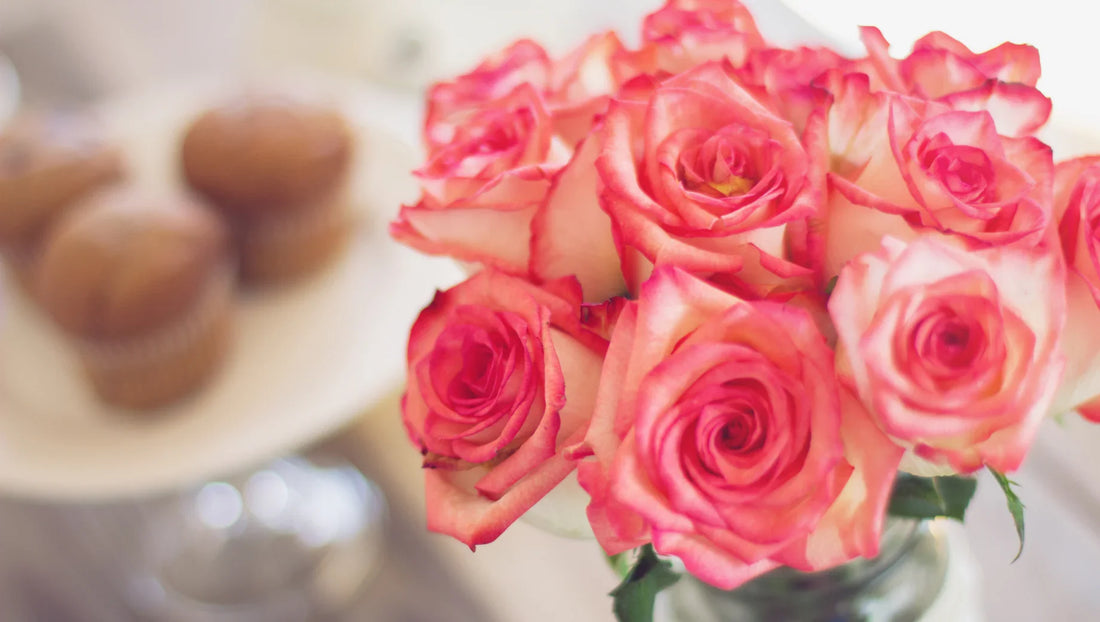 Close-up of pink-edged roses in a vase with blurred muffins on a plate in the background