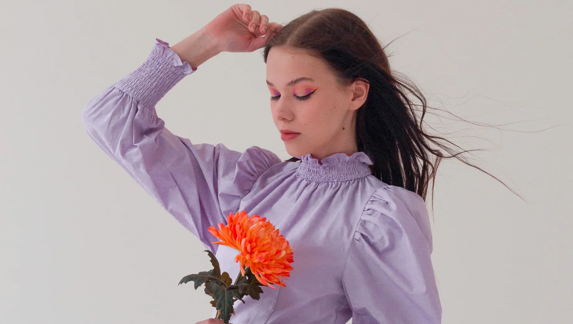 Young woman in a lavender puff-sleeve dress holding a bright orange chrysanthemum flower