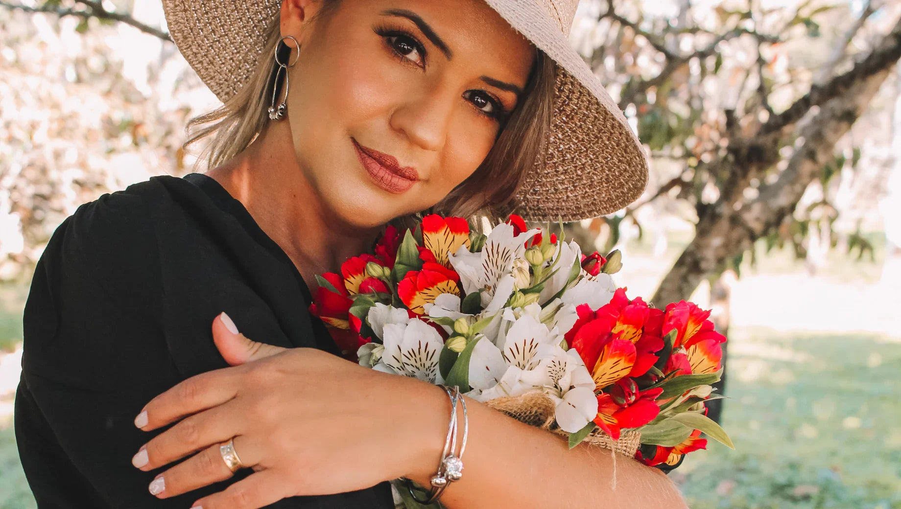 Woman in straw hat holding a bouquet of red and white flowers outdoors in sunlight
