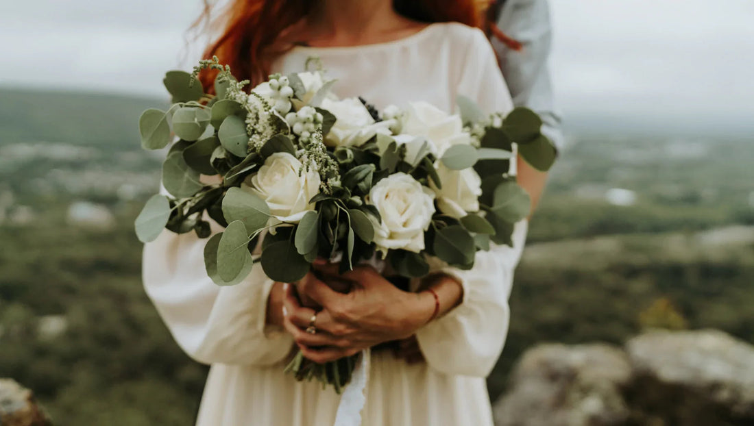 Couple holding white rose and eucalyptus wedding bouquet outdoors with landscape background