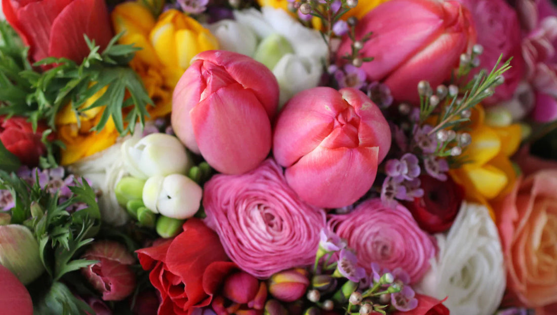 Close-up of colorful spring flowers including pink tulips, ranunculus, roses, and greenery