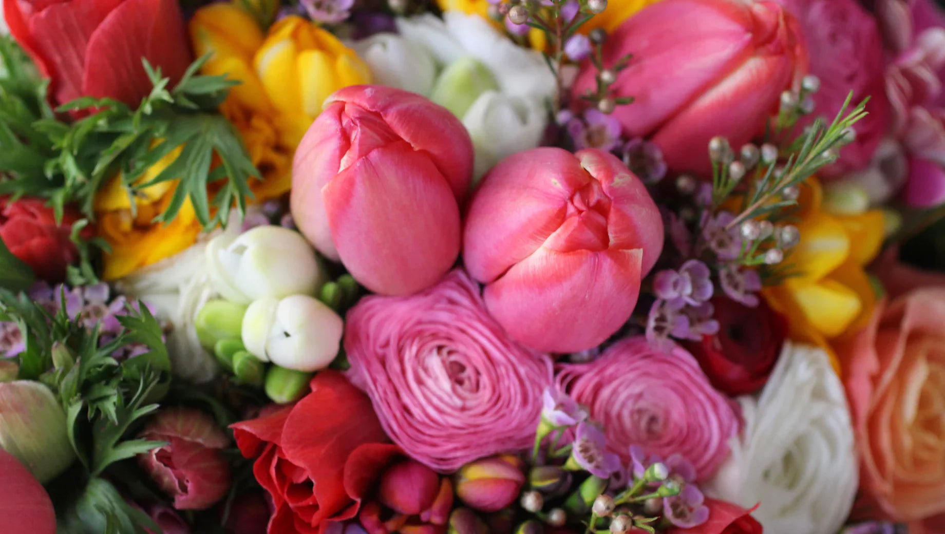 Close-up of colorful spring flowers including pink tulips, ranunculus, roses, and greenery
