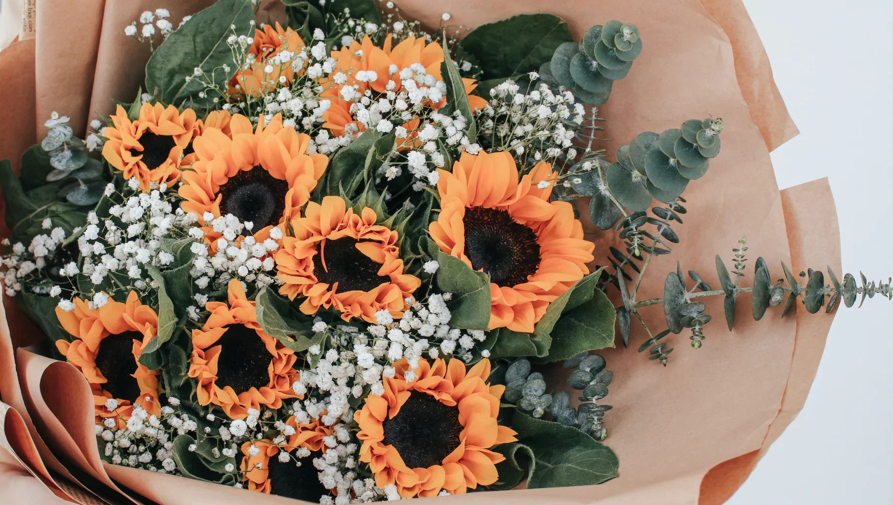 Bouquet of bright orange sunflowers with white baby's breath and eucalyptus wrapped in brown kraft paper