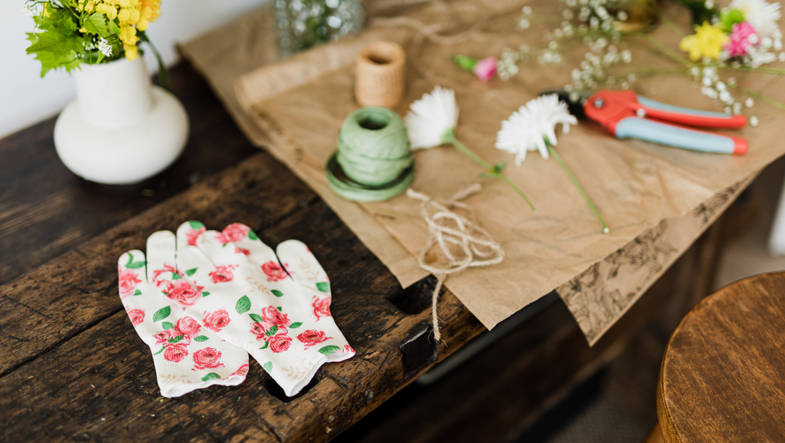 Floral gardening gloves on rustic wooden table with twine, pruners, and fresh flowers