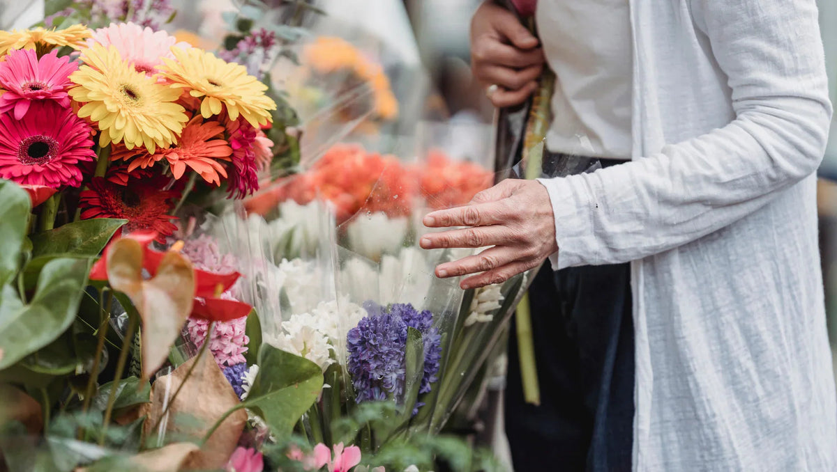 Person in white cardigan browsing colorful flowers at outdoor flower market