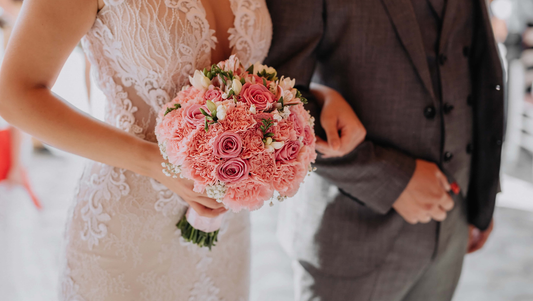 Bride in lace wedding dress holding pink rose and carnation bridal bouquet linked arm with groom in gray suit