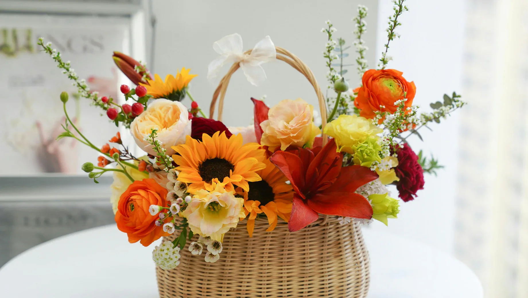Colorful flower arrangement with sunflowers, lilies, and roses in a wicker basket on white table