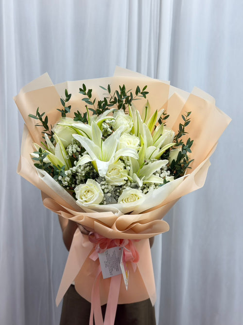 Lily bouquet featuring white and pink lilies arranged with green foliage in a clear glass vase by BestBloomBuddy